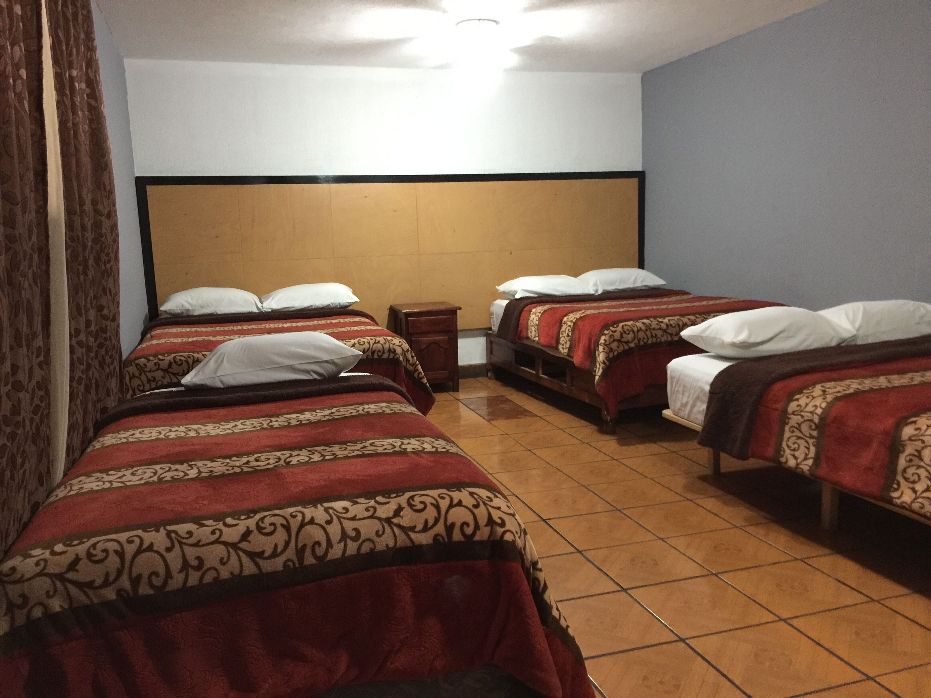 Ein Hotelzimmer mit drei Einzelbetten, jedes mit einer gemusterten Tagesdecke und weißen Kissen.