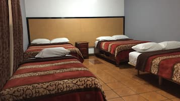 Ein Hotelzimmer mit drei Einzelbetten, jedes mit einer gemusterten Tagesdecke und weißen Kissen.
