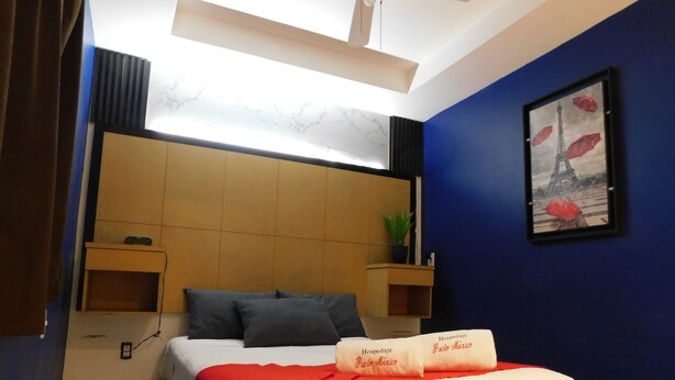 Hotelkamer met een bed, hoofdbord, nachtkastje, wandplank, een ingelijste foto en een plafondventilator.