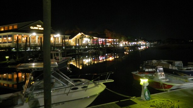 A marina at night with boats docked, a building with illuminated signage, and a calm water surface reflecting the lights. - Beautiful Beach / Golf Villa (Garden City)