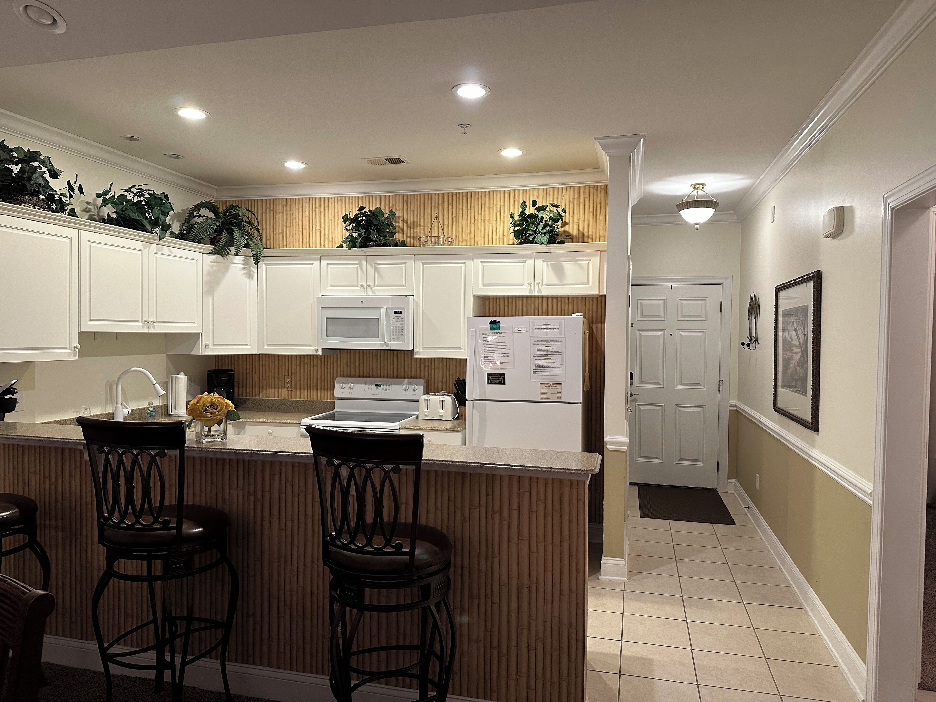 A kitchen with white cabinets, a microwave, a stove, a refrigerator, and a bar area with stools.