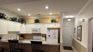 A kitchen with white cabinets, a microwave, a stove, a refrigerator, and a bar area with stools. - Beautiful Beach / Golf Villa (Garden City)