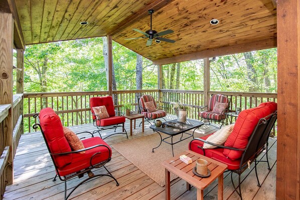 Une terrasse extérieure couverte, avec des chaises rouges et une table, entourée d’arbres.