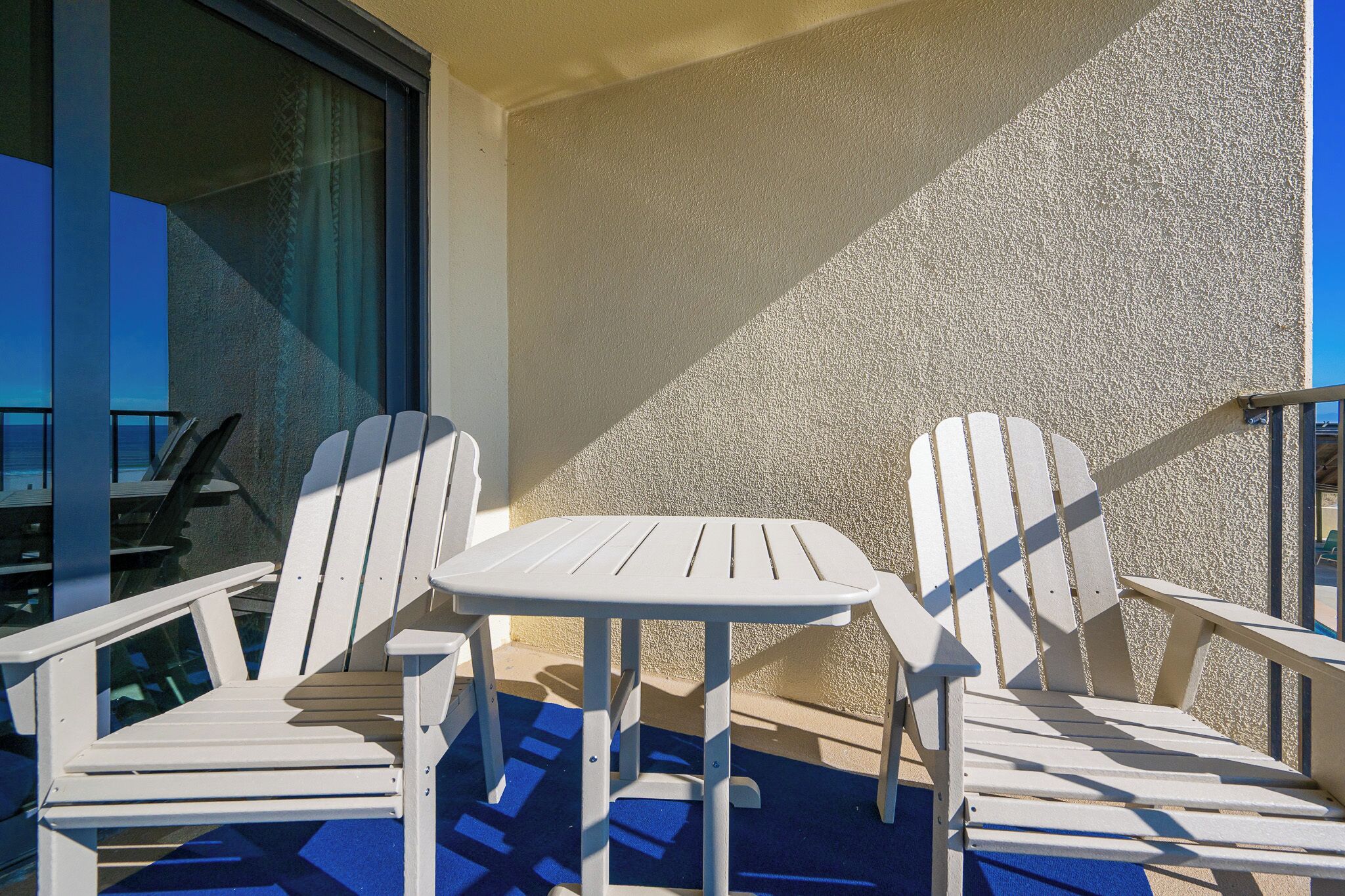 A balcony with two white Adirondack chairs and a small round table.