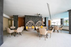 En moderne hotellobby med et siddeområde med runde, vævede stole med hynder, en ventilator i loftet og en væg med geometrisk mønster.