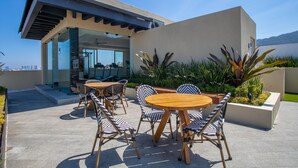 Une terrasse extérieure avec des tables rondes en bois et des chaises à rayures, un bâtiment moderne doté de grandes fenêtres et une vue sur le paysage urbain.