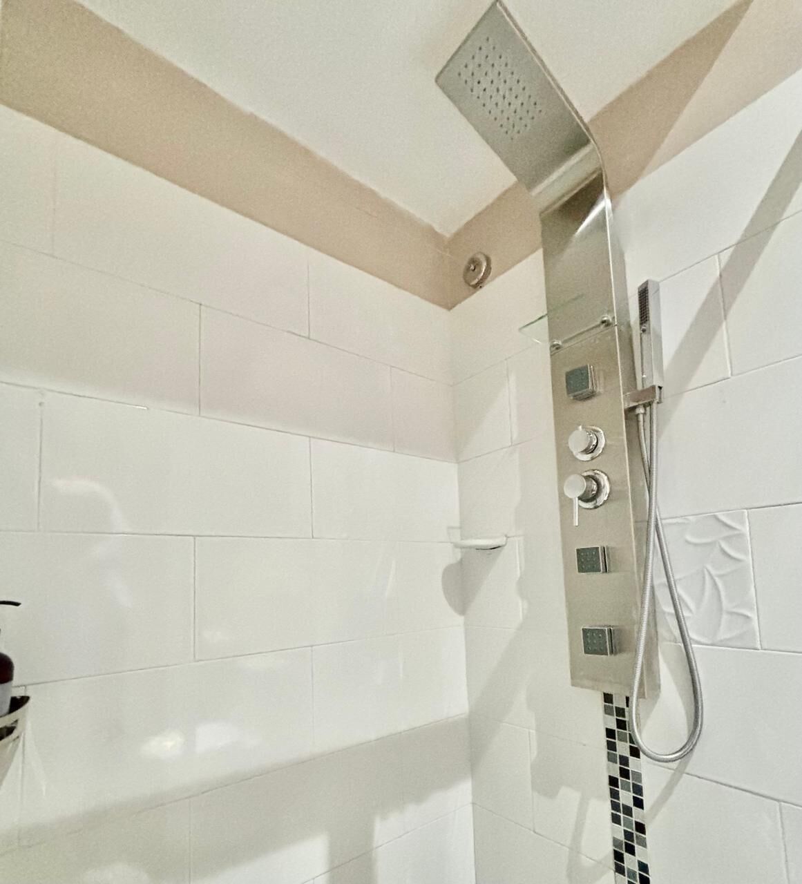 A shower with a handheld showerhead and a wall-mounted control panel.