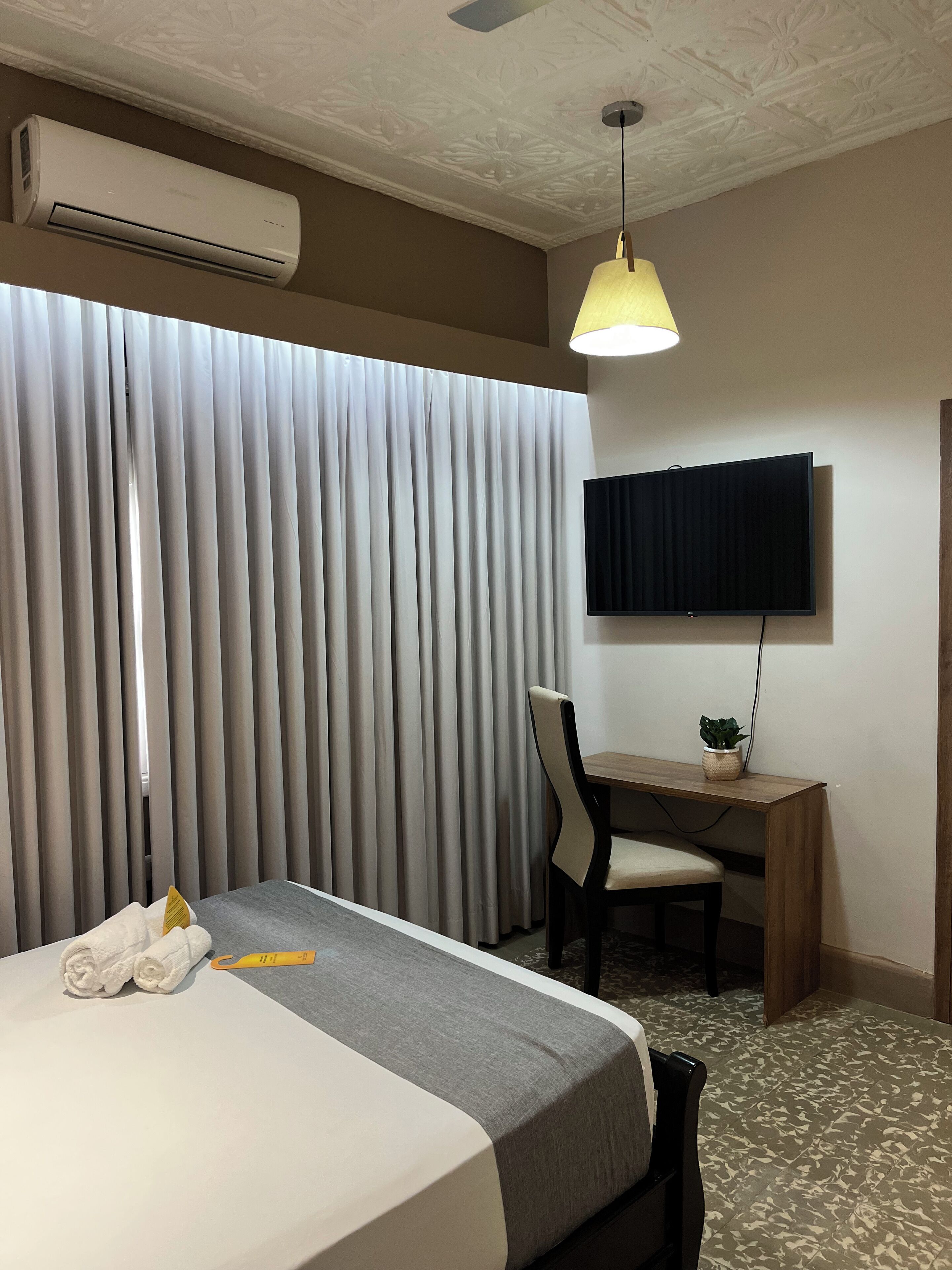 Una habitación de hotel con cama, escritorio, televisor, aire acondicionado y cortina.