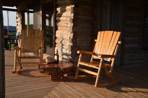 Una mecedora de madera y una silla de madera en una terraza de madera frente a una cabaña de troncos.