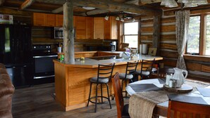 L’intérieur d’un chalet rustique comprend une cuisine, un coin repas et une grande fenêtre à cadre en bois.