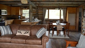 L’intérieur d’un chalet rustique est doté d’un canapé en cuir marron, d’une table à manger en bois et d’un coin cuisine avec un four à micro-ondes.