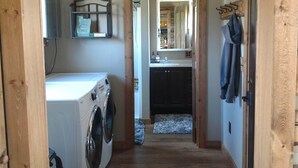 Une buanderie équipée d’un lave-linge et d’un sèche-linge, avec une porte à cadre en bois donnant sur un espace cuisine comprenant un évier et des placards.