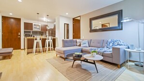 Een moderne woonkamer met een bank, salontafel en een eethoek met barstoelen.