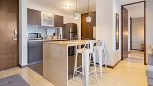 Een moderne keuken met een centraal eiland, barstoelen, een magnetron, een koelkast en hanglampen.