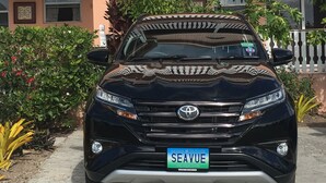 Un'auto Toyota nera parcheggiata di fronte a un edificio con un balcone e un cartello con su scritto "WELCOME".