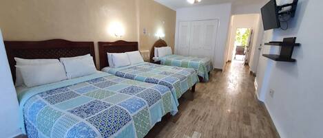 A hotel room with two beds, a ceiling fan, a TV mounted on the wall, and a hallway leading to a door.