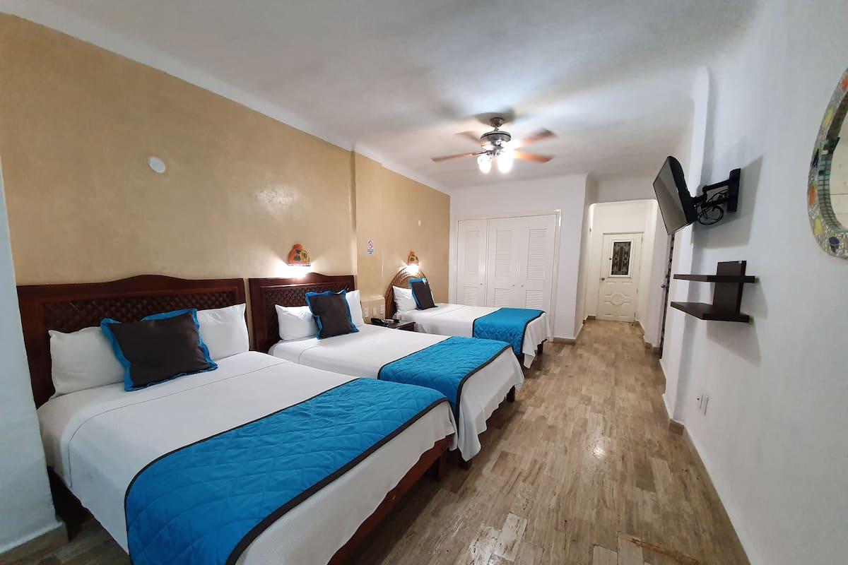 Une chambre d’hôtel avec deux lits, un ventilateur de plafond, un téléviseur fixé au mur et une porte donnant sur une autre chambre.