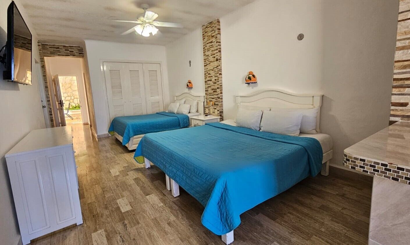 Un dormitorio con dos camas, un armario blanco, ventilador de techo y salpicadero de azulejos.
