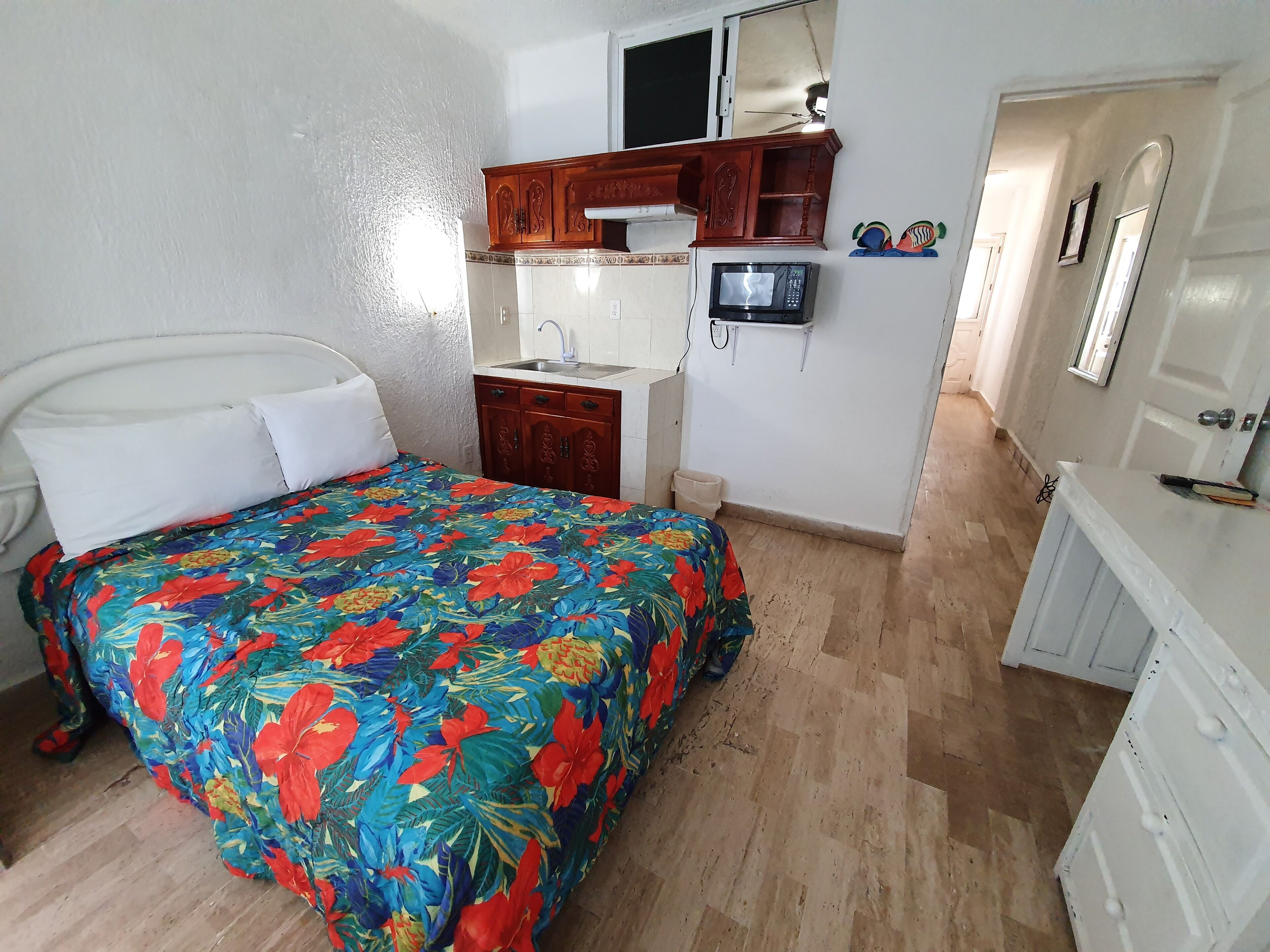 A bedroom with a bed, a small wooden cabinet, a sink, and a television.