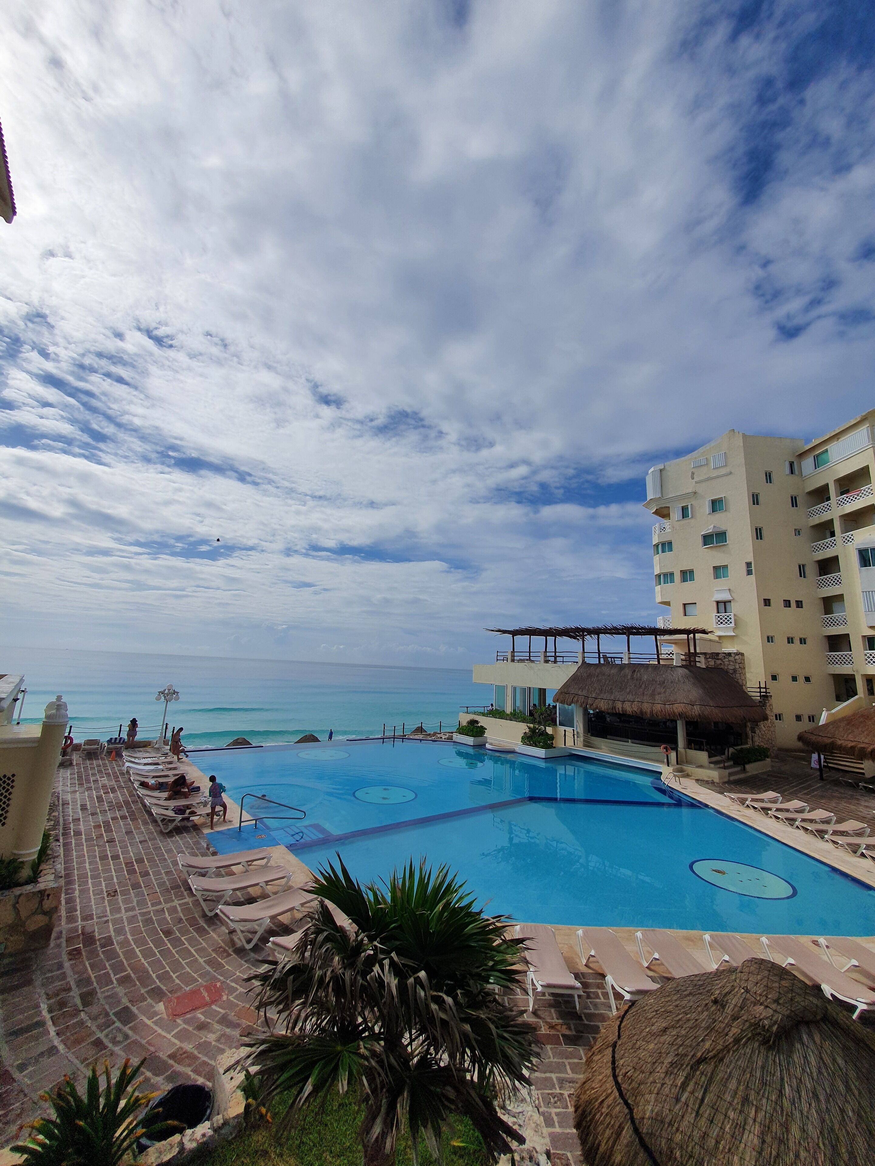 Una piscina di un resort con vista sull'oceano, lettini da relax e un edificio con balconi.