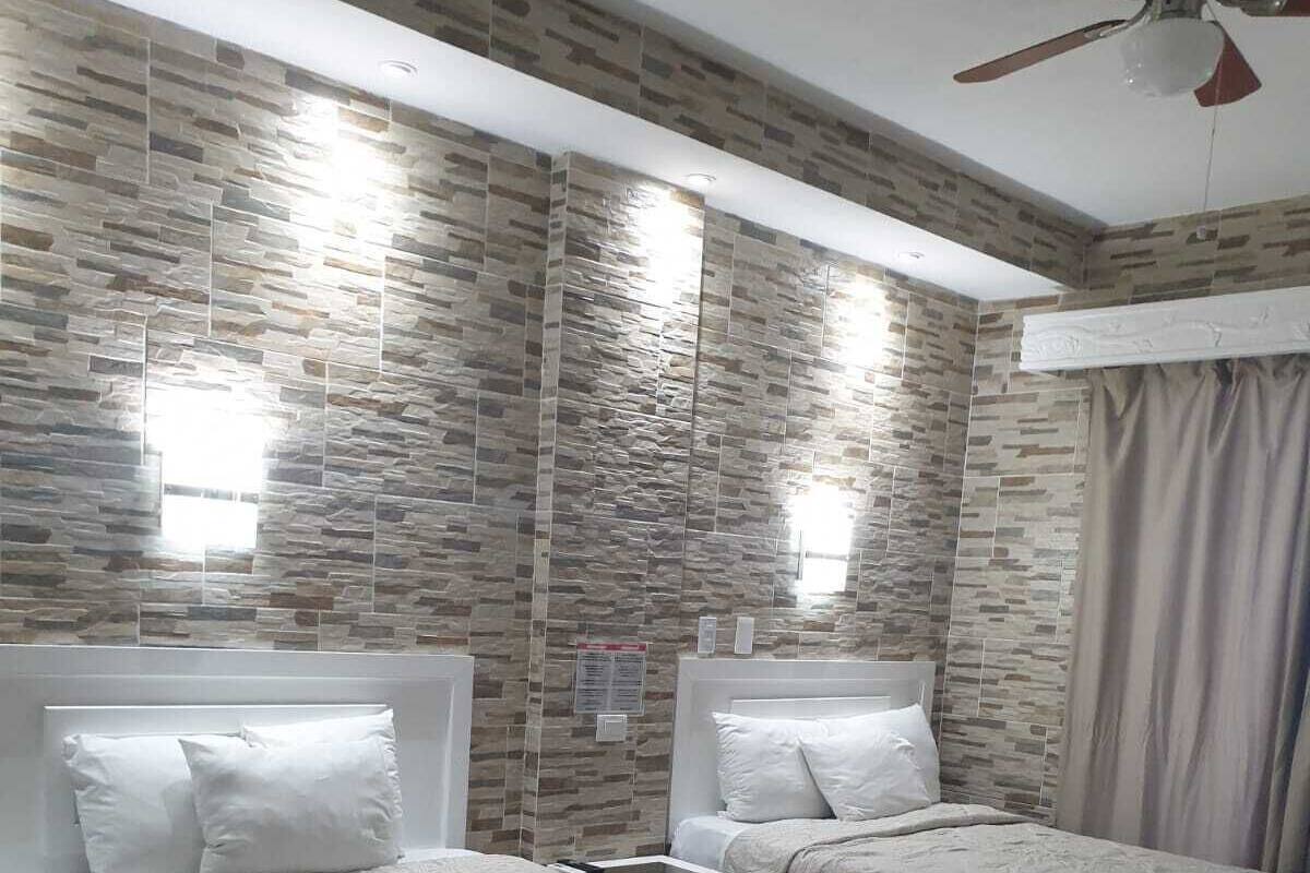 Une chambre d’hôtel avec deux lits, un ventilateur de plafond et un mur décoré d’un motif imitant la pierre.