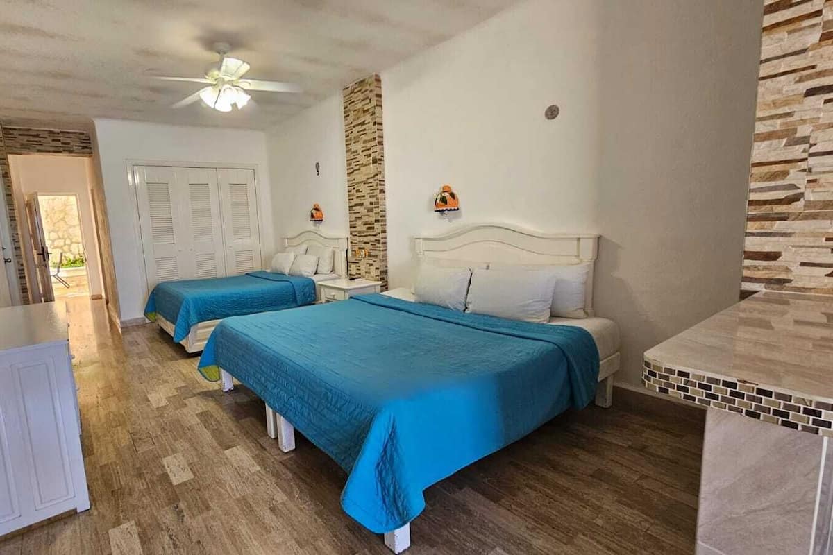 Une chambre d’hôtel avec deux lits, un radiateur blanc, un ventilateur de plafond et un mur décoratif en pierre.