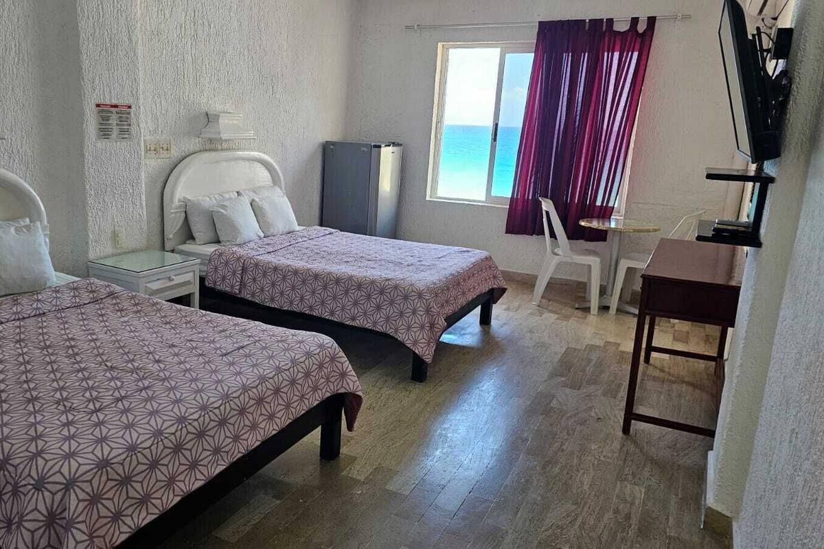 Une chambre avec deux lits, un bureau, une chaise, une télévision et une fenêtre avec des rideaux.