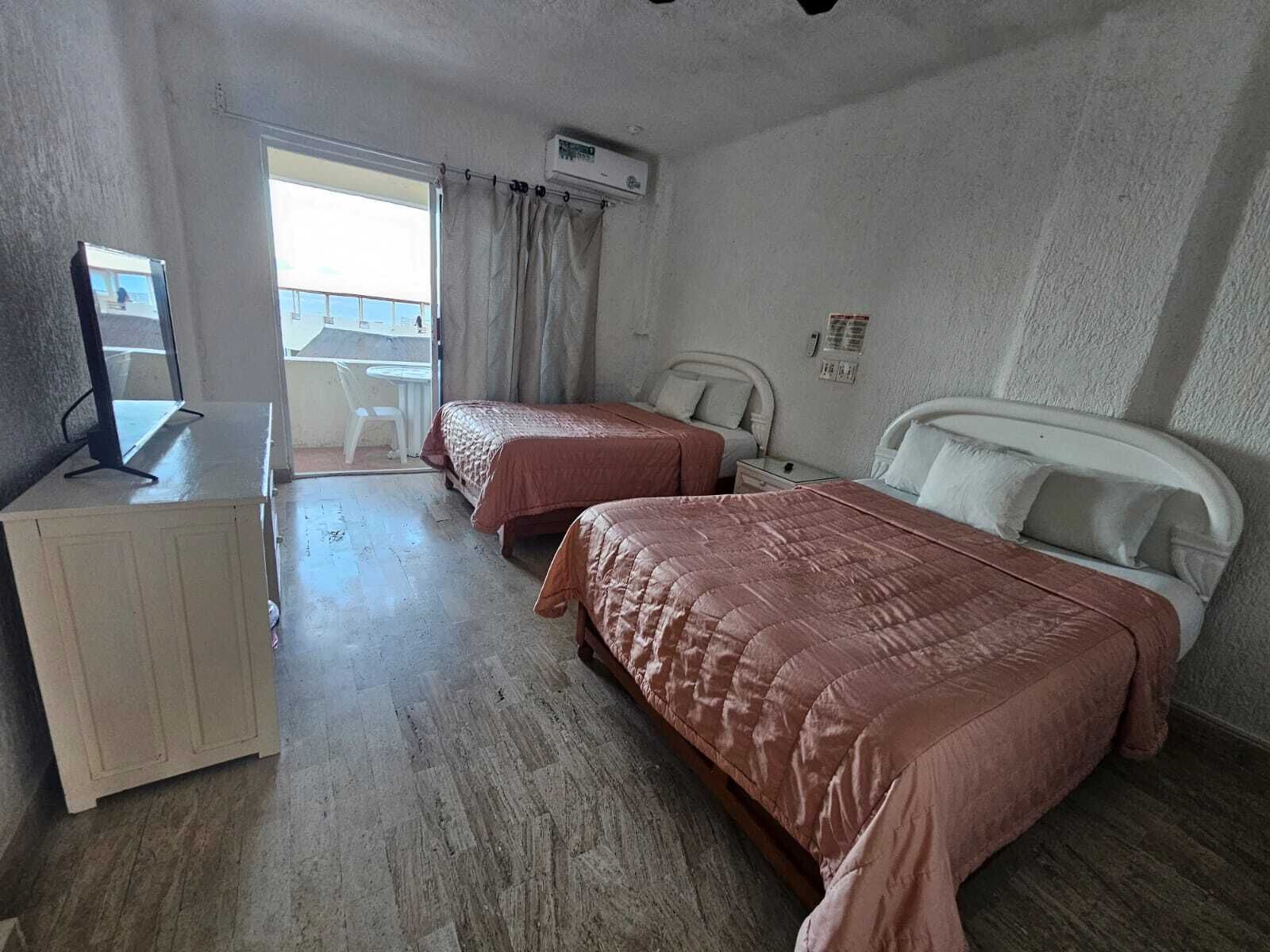 Quarto de hotel com duas camas, uma escrivaninha e uma janela com cortinas.