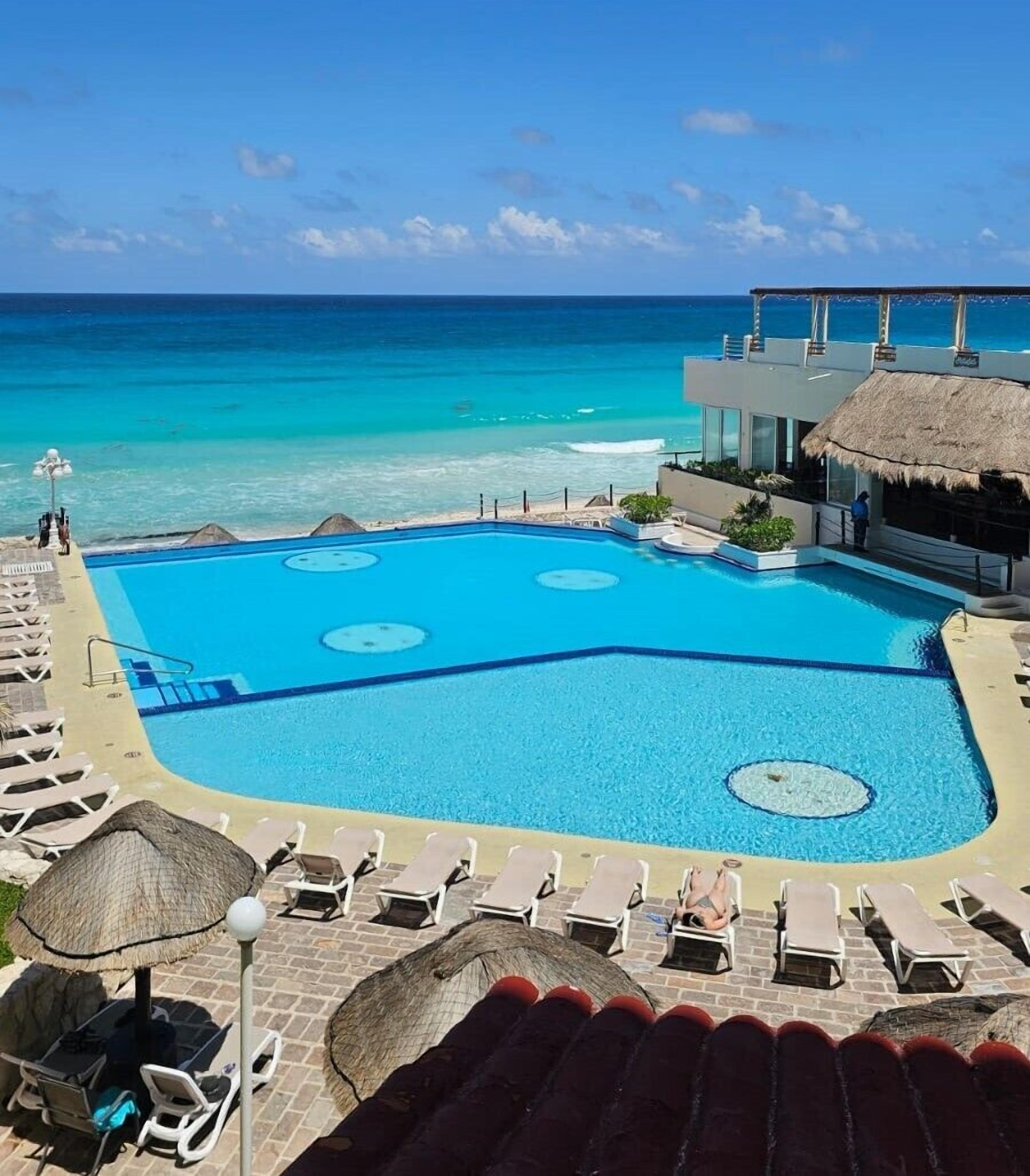 Une piscine avec vue sur l’océan, des chaises longues et un bâtiment doté d’un toit de chaume.