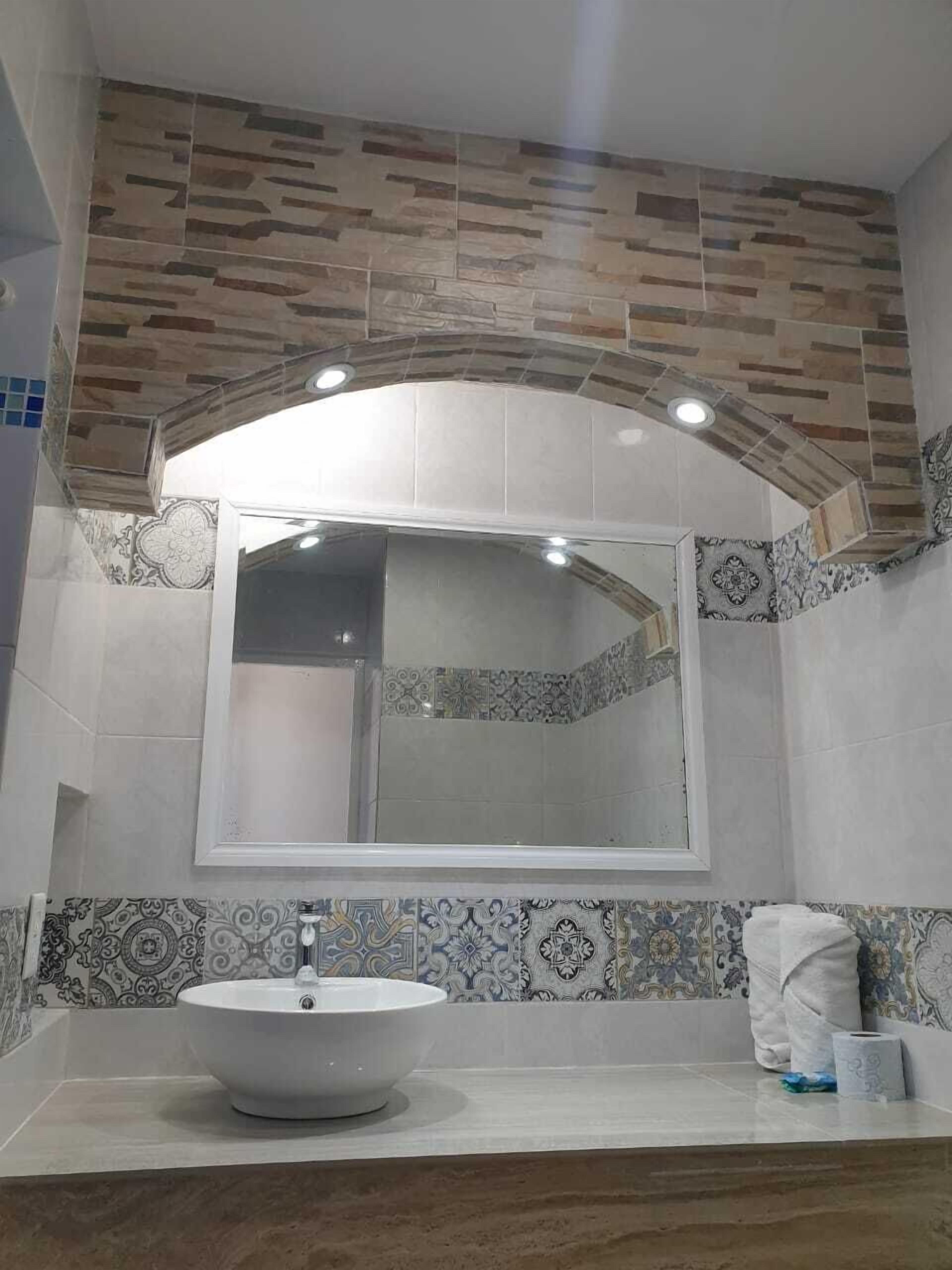 A bathroom with a large mirror, a white sink, patterned tiles, and a towel on the counter.