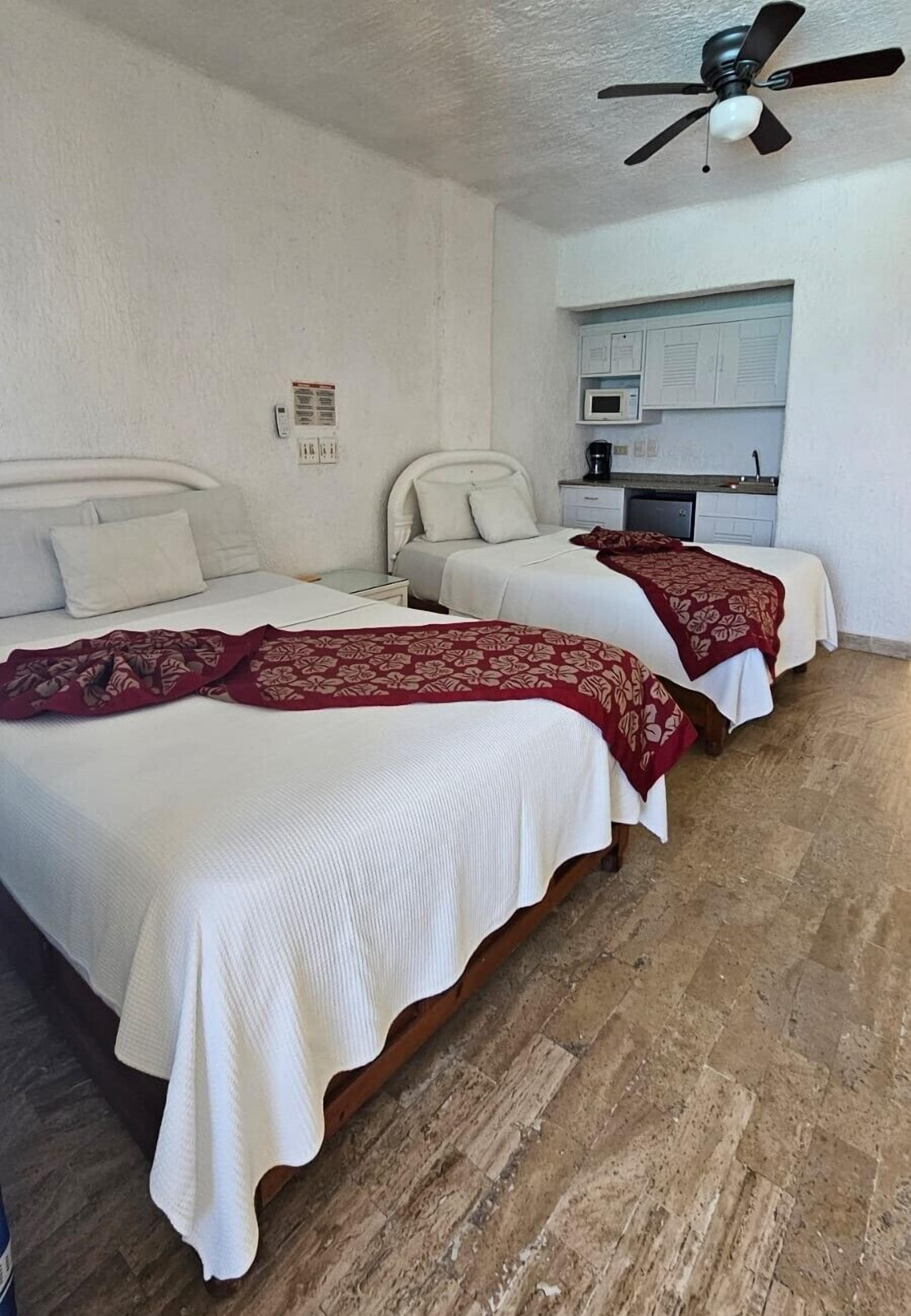 Habitación de hotel con dos camas, ventilador de techo, microondas y una pequeña kitchenette.