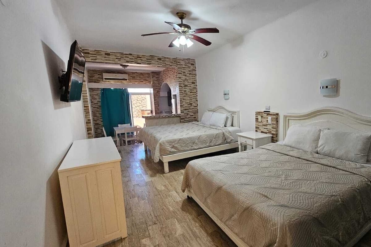 Une chambre avec deux lits, un ventilateur de plafond, une armoire en bois et un mur en pierre.
