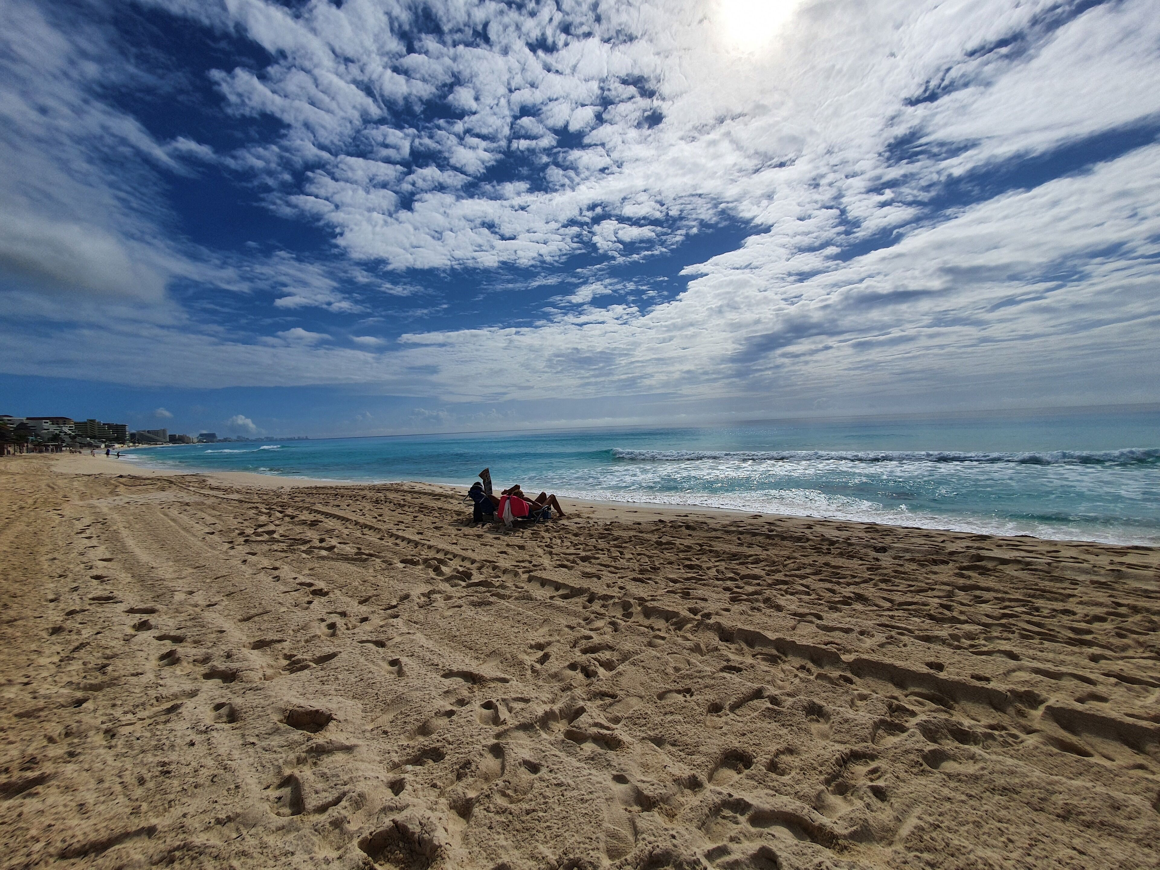 A beach with footprints leading to a group of people sitting on the sand.