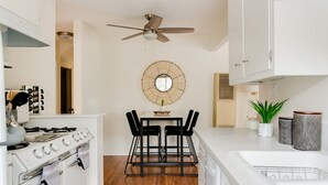Una cucina moderna con mobili bianchi, un piano cottura a gas, una ventola a soffitto e una zona pranzo con uno specchio rotondo sopra il tavolo.