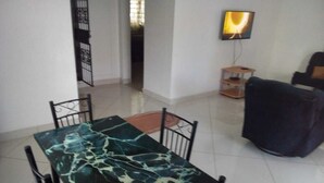 A dining area with a marble table and chairs, a television on the wall, and a sofa in the background. - SHREE ENCLAVE WEST COURT (Mombasa)