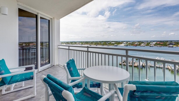 A balcony with white chairs and a table, overlooking a marina with boats and a distant shoreline. - Trendy & Tranquil! (Pensacola)