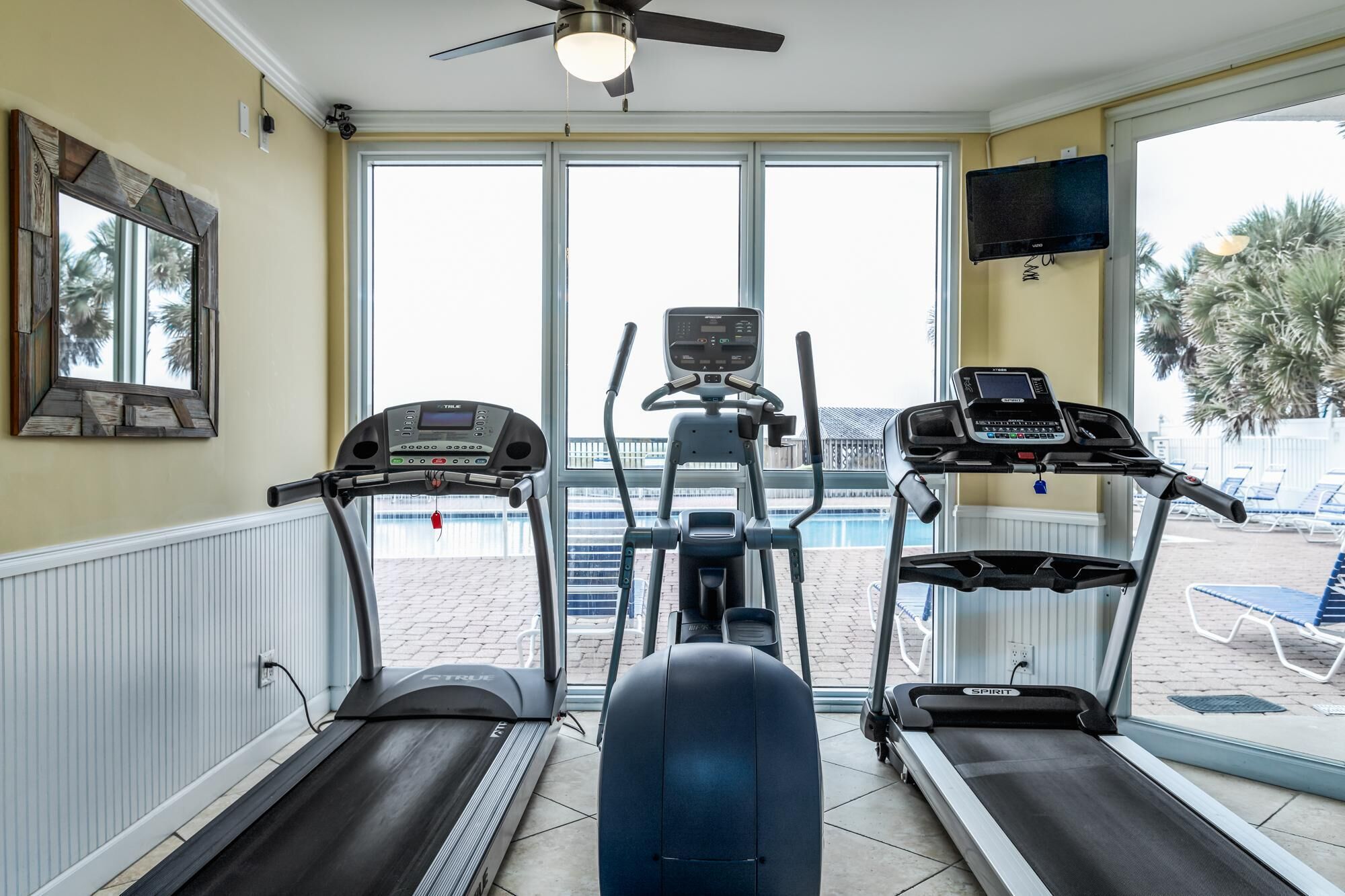 A fitness room with three treadmills, a ceiling fan, and a TV mounted on the wall.