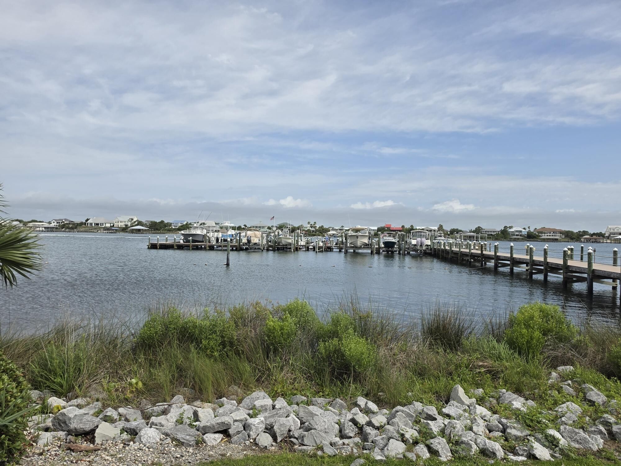 Un puerto deportivo con barcos amarrados, un muelle que se adentra en el agua y edificios residenciales al fondo.