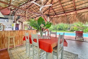Un espace de restauration en plein air doté d’un toit de chaume, d’une piscine et d’un bar en bois.