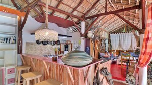 A rustic interior with a thatched roof, wooden furniture, and a central bar area.