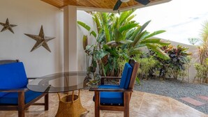 A covered patio with two blue chairs, a glass table, and a ceiling fan. - Private Garden, Walk Out to Community Pool, Beautiful 1 Bedroom 1 Bath Condo (San Buenas)