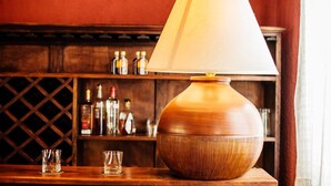 Una mesa de madera con una lámpara, dos vasos y una estantería con botellas al fondo.