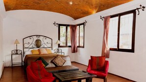 Un dormitorio con techo de madera, una cama con cabecera, una mesa de madera, dos sillas y una ventana con cortinas.