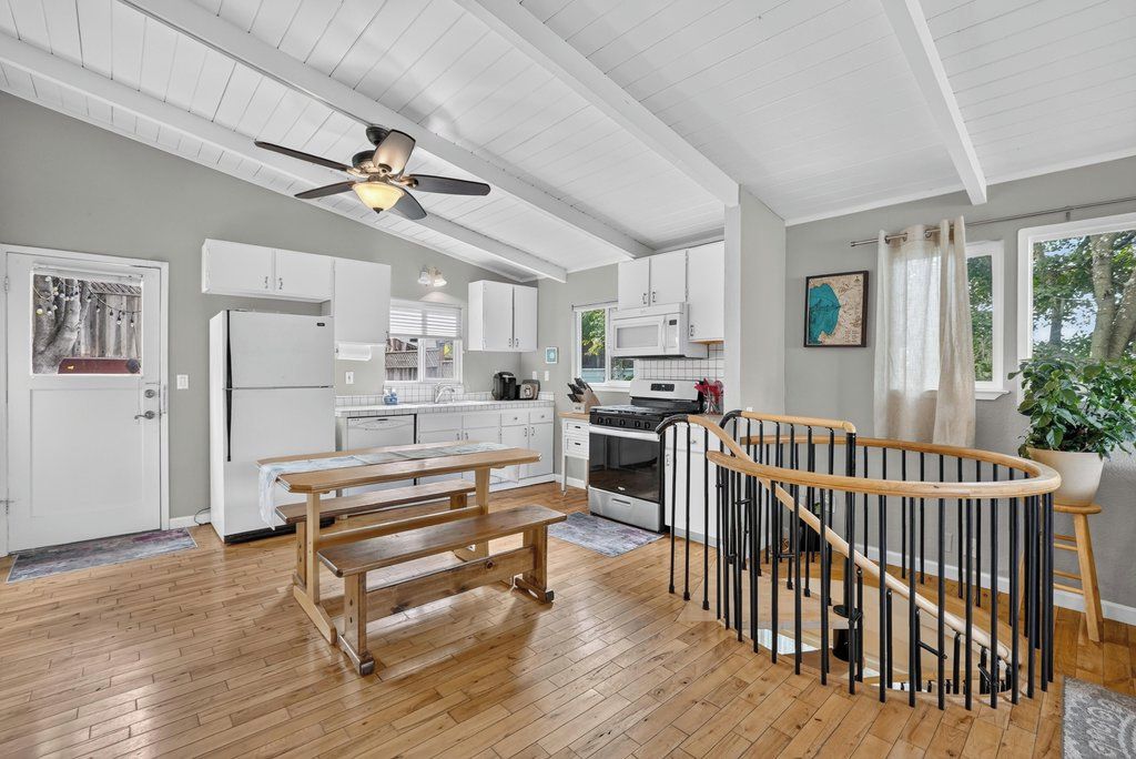 A modern kitchen with white cabinets, a wooden bench, and a spiral staircase.