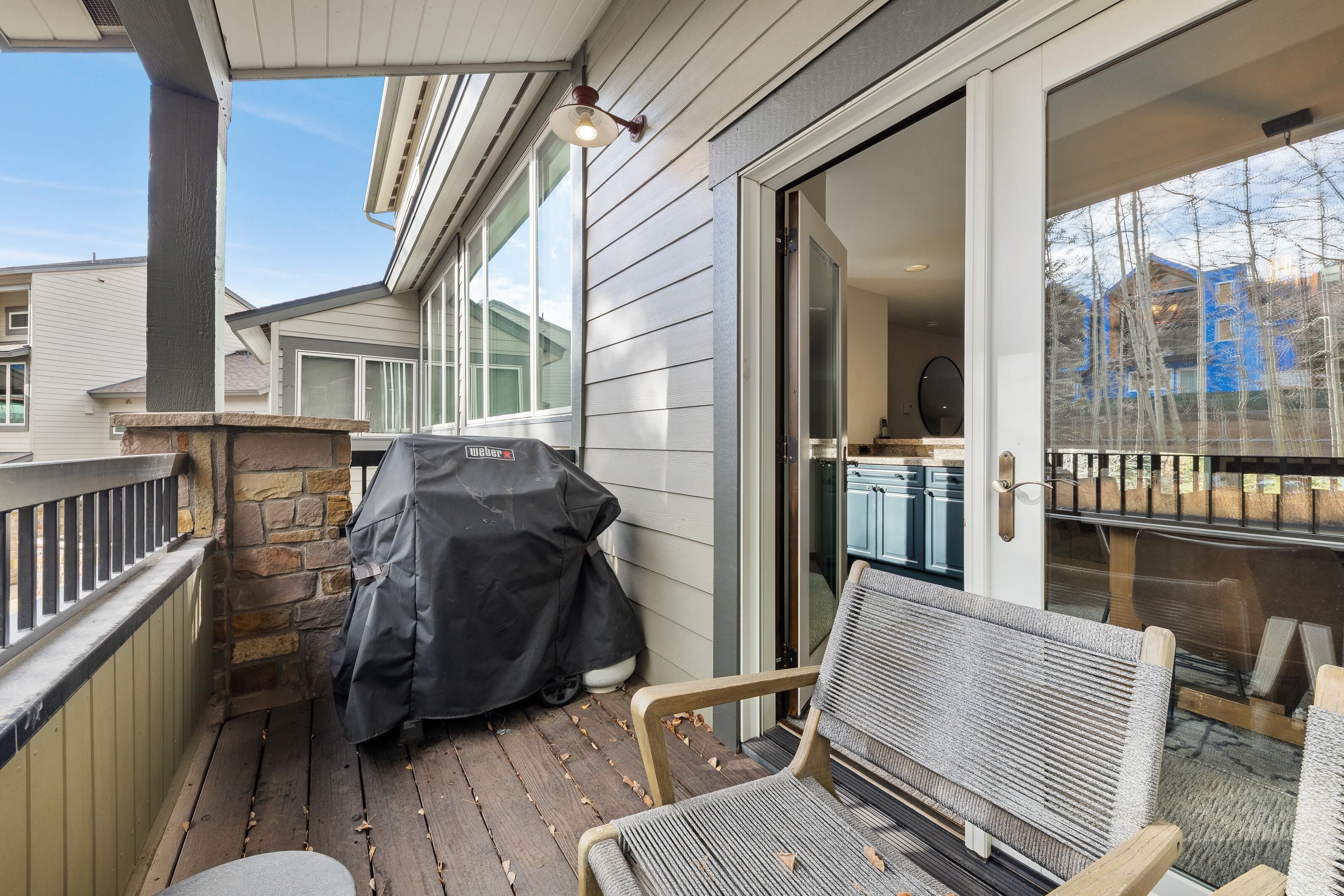 A covered outdoor area with a grill, a chair, and a sliding glass door leading to a kitchen.
