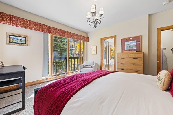 Ein Schlafzimmer mit einem großen Bett, einem Schreibtisch, einem Stuhl, einer Kommode und einem Fenster mit Blick auf Bäume.