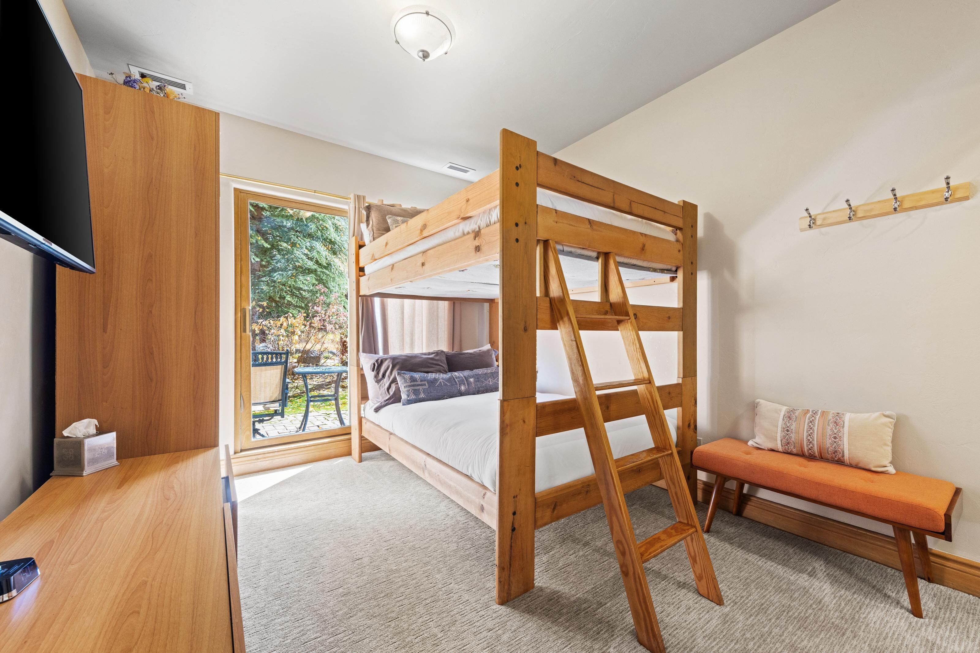 A bunk bed with a ladder, a wooden desk, a bench, and a television.
