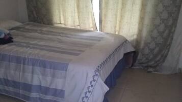 A bedroom with a bed, curtains, and a tiled floor.