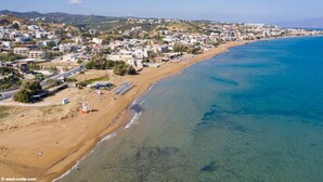Une vue aérienne d’une ville côtière avec une plage, des eaux d’un bleu limpide et un mélange de bâtiments résidentiels.