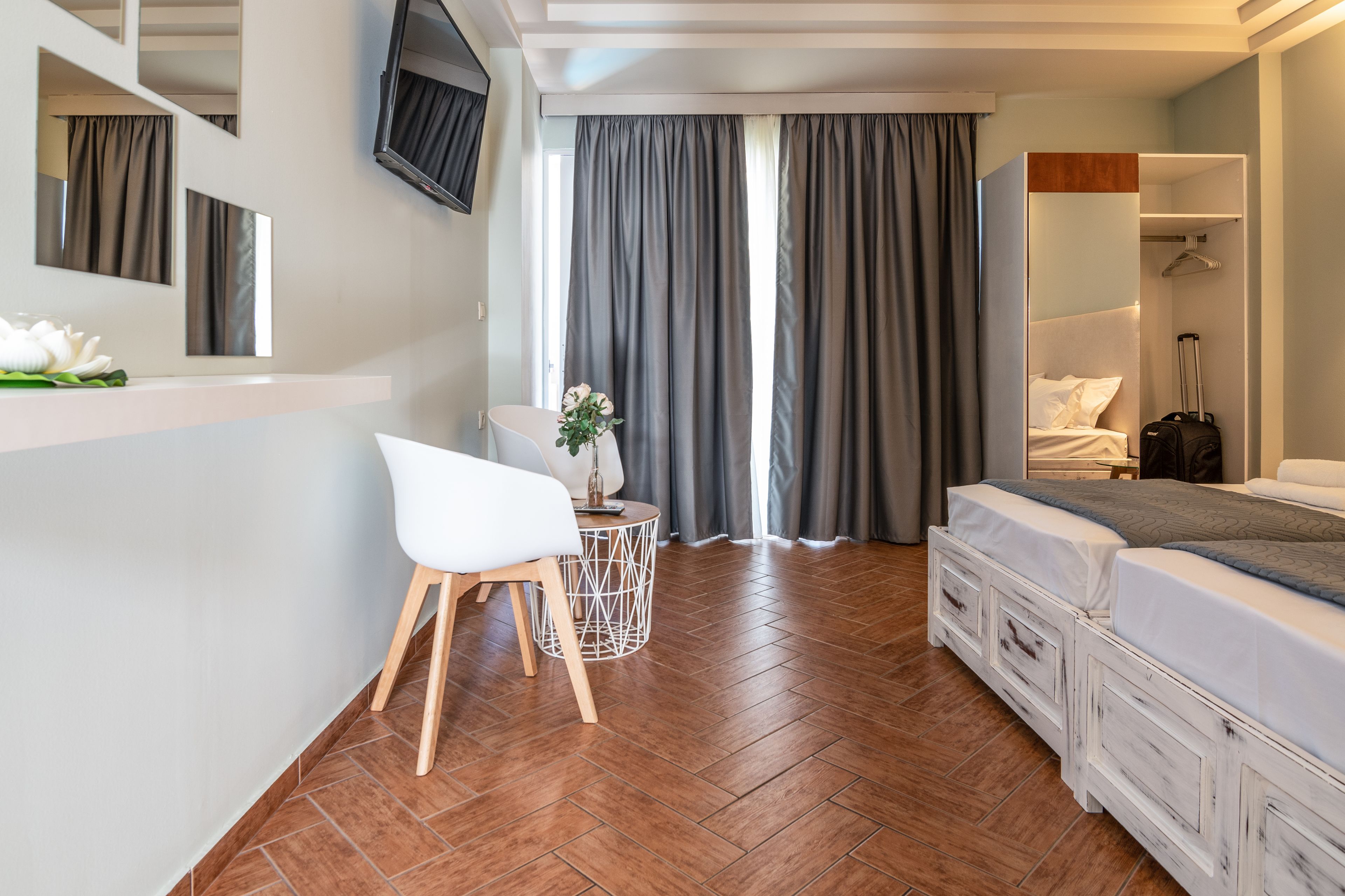 Et moderne hotelværelse med trægulv, en hvid seng, et rundt bord med en stol, et spejl og et fjernsyn ophængt på væggen.